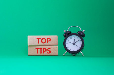 Top Tips symbol. Concept words Top Tips on wooden blocks. Beautiful green background with alarm...