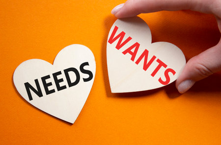 Wants and Needs symbol. Concept word Wants and Needs on wooden hearts. Businessman hand. Beautiful orange background. Business and Wants and Needs concept. Copy spaceの写真素材