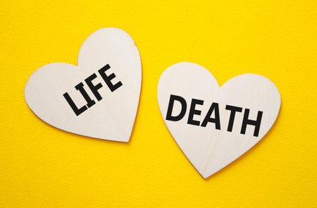 Life or Death symbol. Concept word Life or Death on wooden hearts. Beautiful yellow background. Business and Life or Death concept. Copy spaceの写真素材