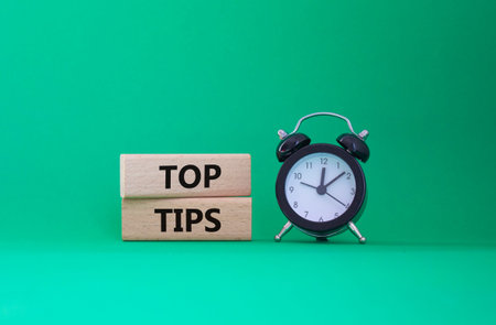 Top Tips symbol. Concept words Top Tips on wooden blocks. Beautiful green background with alarm...