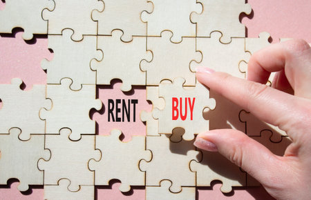 Rent or Buy symbol. Concept word Rent or Buy on wooden puzzle. Businessman hand. Beautiful pink background. Business and Rent or Buy concept. Copy spaceの写真素材