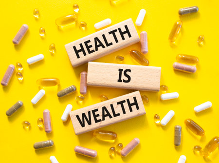 Health is Wealth symbol. Concept word Health is Wealth on wooden blocks. Beautiful yellow background with pills. Medicine and Health is Wealth concept. Copy spaceの写真素材