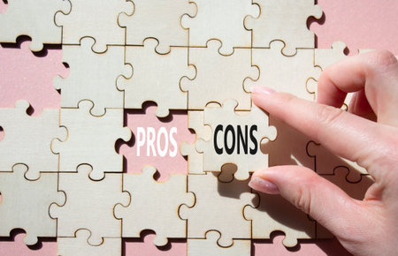 Pros vs Cons symbol. Concept word Pros vs Cons on wooden puzzle. Businessman hand. Beautiful pink background. Business and Pros vs Cons concept. Copy spaceの写真素材