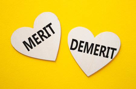 Merit or Demerit symbol. Concept word Merit or Demerit on wooden hearts. Beautiful yellow background. Business and Merit or Demerit concept. Copy spaceの写真素材