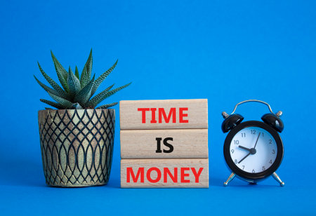 Time is Money symbol. Concept words Time is Money on wooden blocks. Beautiful blue background with alarm clock and succulent plant. Business and Time is Money concept. Copy spaceの写真素材