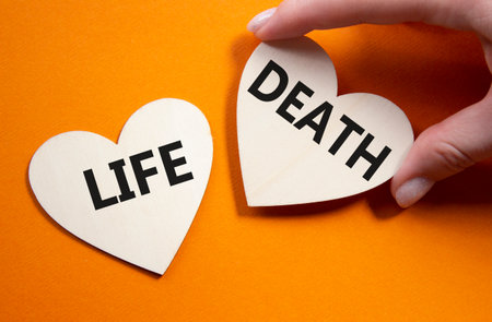 Life or Death symbol. Concept word Life or Death on wooden hearts. Businessman hand. Beautiful orange background. Business and Life or Death concept. Copy spaceの写真素材