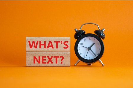 What is next symbol. Concept words What is next on wooden blocks. Beautiful orange background with alarm clock. Business and What is next concept. Copy space.の写真素材