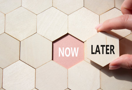 Now vs Later symbol. Concept word Now vs Later on wooden comb puzzle. Businessman hand. Beautiful pink background. Business and Now vs Later concept. Copy spaceの写真素材