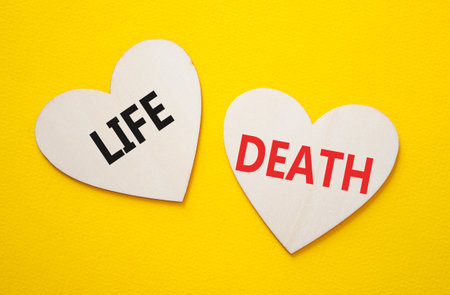 Life or Death symbol. Concept word Life or Death on wooden hearts. Beautiful yellow background. Business and Life or Death concept. Copy spaceの写真素材