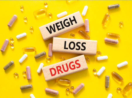 Medicine symbol. Concept words Weight Loss Drugs on wooden blocks. Beautiful yellow background with pills. Medicine concept and Weight Loss Drugs. Copy spaceの写真素材