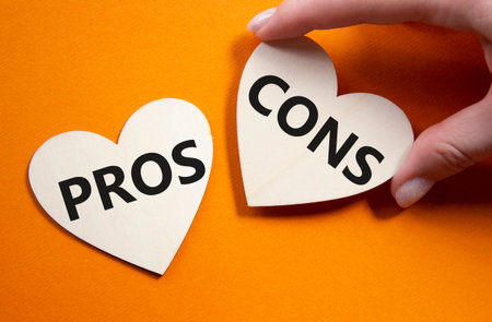 Pros vs Cons symbol. Concept word Pros vs Cons on wooden hearts. Businessman hand. Beautiful orange background. Business and Pros vs Cons concept. Copy spaceの写真素材