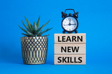 Learn new skills symbol. Concept words Learn new skills on wooden blocks. Beautiful blue background with succulent plant and alarm clock. Business and Learn new skills concept. Copy space.の写真素材