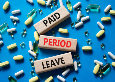 Paid Period Leave symbol. Concept words Paid Period Leave on wooden blocks. Beautiful blue background with pills. Healthcare and Paid Period Leave concept. Copy space.の写真素材
