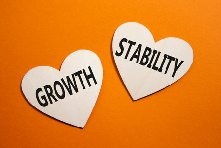 Growth and Stability symbol. Concept word Growth and Stability on wooden hearts. Beautiful orange background. Business and Growth and Stability concept. Copy spaceの写真素材