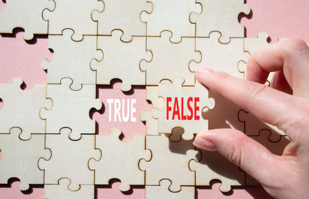 True or False symbol. Concept word True or False on wooden puzzle. Businessman hand. Beautiful pink...