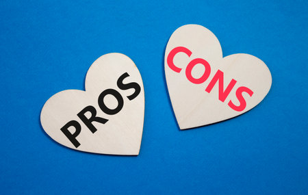 Pros vs Cons symbol. Concept word Pros vs Cons on wooden hearts. Beautiful blue background. Business and Pros vs Cons concept. Copy spaceの写真素材