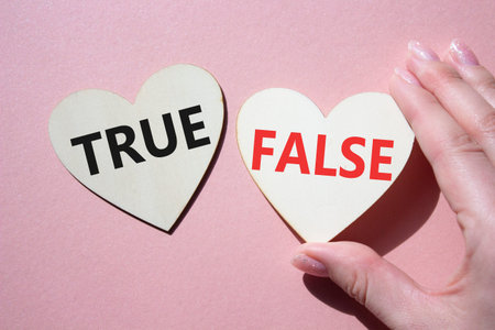 True or False symbol. Concept word True or False on wooden hearts. Businessman hand. Beautiful pink...