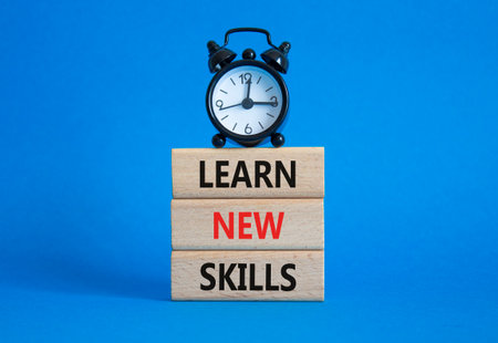 Learn new skills symbol. Concept words Learn new skills on wooden blocks. Beautiful blue background with alarm clock. Business and Learn new skills concept. Copy space.の写真素材