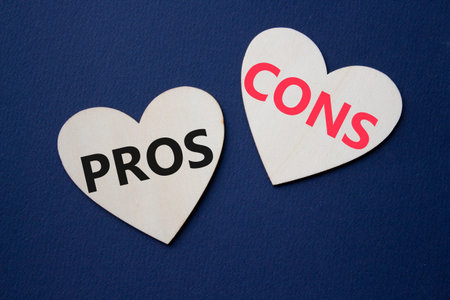 Pros vs Cons symbol. Concept word Pros vs Cons on wooden hearts. Beautiful deep blue background....