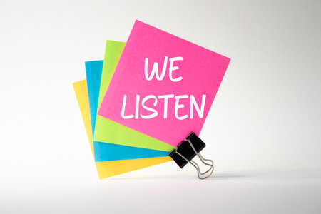 Pink sticky note with words We listen. Beautiful white background. Business concept. Copy space.の写真素材