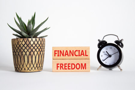 Financial freedom symbol. Wooden blocks with words Financial freedom. Beautiful white background with alarm clock and succulent plant. Business and Financial freedom concept. Copy space.の写真素材