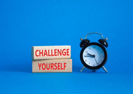 Challenge yourself symbol. Wooden blocks with words Challenge yourself. Beautiful blue background with alarm clock. Business and Challenge yourself concept. Copy space.の写真素材