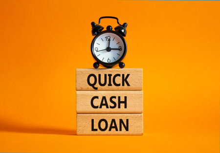 Quick Cash Loan symbol. Concept words Quick Cash Loan on wooden blocks. Beautiful orange background with alarm clock. Business and Quick Cash Loan concept. Copy space.の写真素材