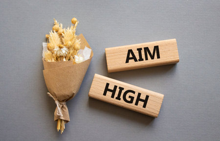 Aim High symbol. Wooden blocks with words Aim High. Beautiful gray background with bouquet of flowers. Business and Aim High concept. Copy space.の写真素材