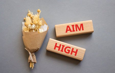 Aim High symbol. Wooden blocks with words Aim High. Beautiful gray background with bouquet of flowers. Business and Aim High concept. Copy space.の写真素材