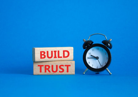 Build trust symbol. Wooden blocks with words Build trust. Beautiful blue background with alarm clock. Business and Build trust concept. Copy space.の写真素材