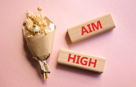 Aim High symbol. Wooden blocks with words Aim High. Beautiful pink background with bouquet of flowers. Business and Aim High concept. Copy space.の写真素材