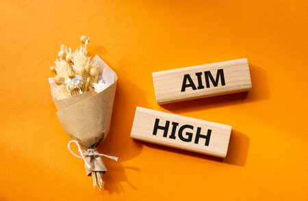 Aim High symbol. Wooden blocks with words Aim High. Beautiful orange background with bouquet of flowers. Business and Aim High concept. Copy space.の写真素材