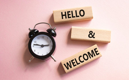 Hello and Welcome symbol. Concept words Hello and Welcome on wooden blocks. Beautiful pink background with alarm clock. Business and Hello and Welcome concept. Copy space.の写真素材