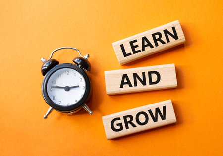 Learn and grow symbol. Concept words Learn and grow on wooden blocks. Beautiful orange background with alarm clock. Business and Learn and grow concept. Copy space.の写真素材