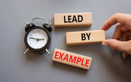 Lead by Example symbol. Concept word Lead by Example on wooden cubes. Businessman hand. Beautiful gray background with alarm clock. Business and Lead by Example concept. Copy space.の写真素材