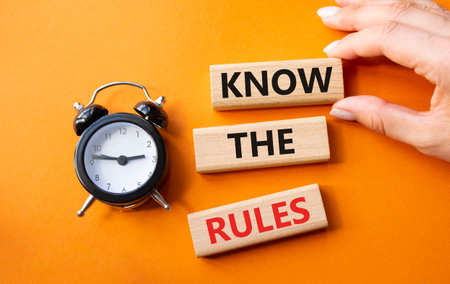 Know the rules symbol. Wooden blocks with words Know the rules. Businessman hand. Beautiful orange background with alarm clock. Business and Know the rules concept. Copy space.の写真素材