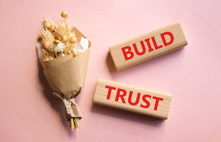Build trust symbol. Wooden blocks with words Build trust. Beautiful pink background with bouquet of flowers. Business and Build trust concept. Copy space.の写真素材
