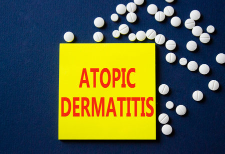 Atopic Dermatitis symbol. Concept word Atopic Dermatitis on yellow note. Beautiful deep blue background with pills. Medicine and Atopic Dermatitis concept. Copy spaceの写真素材