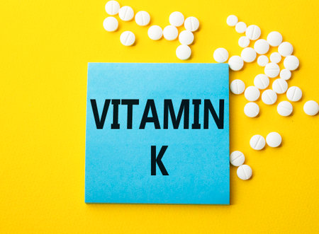 Vitamin K symbol. Concept word Vitamin K on blue note. Beautiful yellow background with pills. Medicine and Vitamin K concept. Copy spaceの写真素材