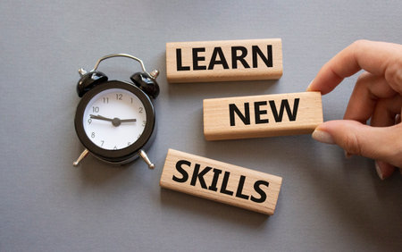 Learn new skills symbol. Concept words Learn new skills on wooden blocks. Businessman hand. Beautiful gray background with alarm clock. Business and Learn new skills concept. Copy space.の写真素材