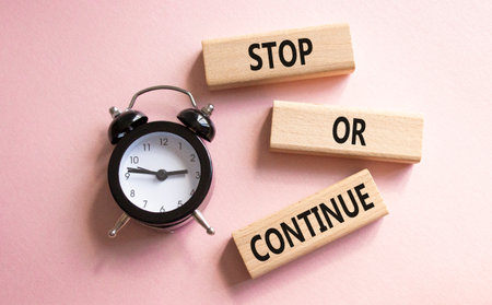 Stop or Continue symbol. Concept words Stop or Continue on wooden blocks. Beautiful pink background with alarm clock. Business concept and Stop or Continue. Copy space.の写真素材
