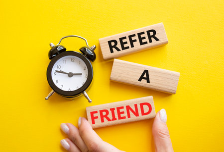 Refer a Friend symbol. Concept words Refer a Friend on wooden blocks. Businessman hand. Beautiful yellow background with alarm clock. Business and Refer a Friend concept. Copy space.の写真素材