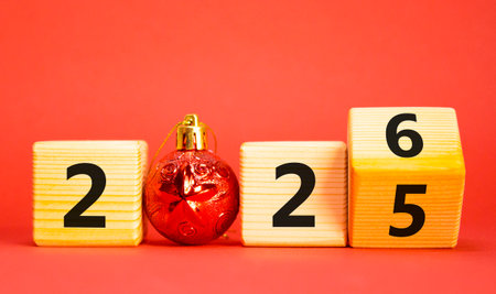 2026 New Year symbol. Businessman turns wooden cube and changes Year 2025 to 2026. Beautiful red background with christmas ball. Copy space. Business and 2026 happy new year conceptの写真素材