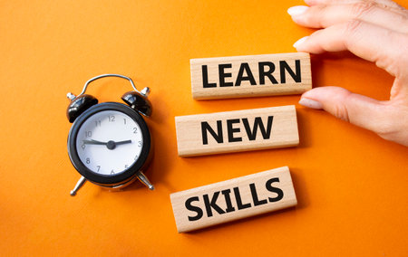 Learn new skills symbol. Concept words Learn new skills on wooden blocks. Businessman hand. Beautiful orange background with alarm clock. Business and Learn new skills concept. Copy space.の写真素材