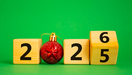 2026 New Year symbol. Businessman turns wooden cube and changes Year 2025 to 2026. Beautiful green background with Christmas ball. Copy space. Business and 2026 happy new year conceptの写真素材