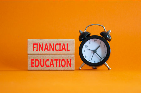 Financial Education symbol. Wooden blocks with words Financial Education. Beautiful orange background with alarm clock. Business and Financial Education concept. Copy space.の写真素材