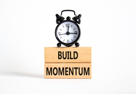 Build momentum symbol. Wooden blocks with words Build momentum. Beautiful white background with alarm clock. Business and Build momentum concept. Copy space.の写真素材