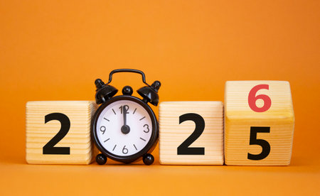 2026 New Year symbol. Businessman turns wooden cube and changes Year 2025 to 2026. Beautiful orange background with Alarm clock. Copy space.の写真素材