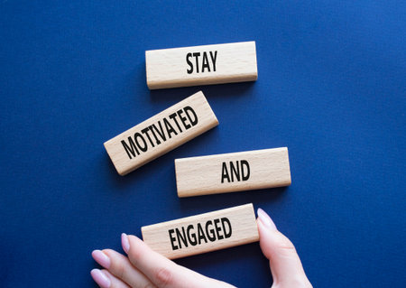 Stay Motivated and Engaged symbol. Concept words Stay Motivated and Engaged on wooden blocks. Beautiful deep blue background. Businessman hand. Business concept. Copy spaceの写真素材