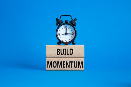 Build momentum symbol. Wooden blocks with words Build momentum. Beautiful blue background with alarm clock. Business and Build momentum concept. Copy space.の写真素材